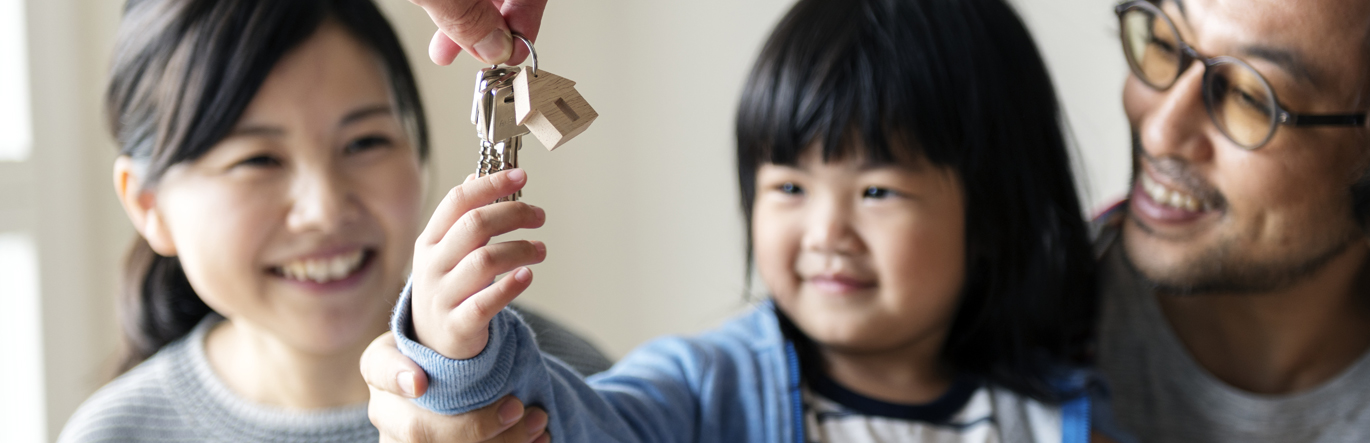 A couple watches, smiling as their toddler daughter grabs keys to a home