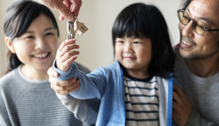 A couple watches, smiling as their toddler daughter grabs keys to a home