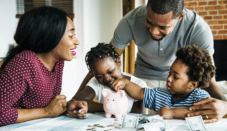 A family teaches their toddlers to put money in a piggy bank