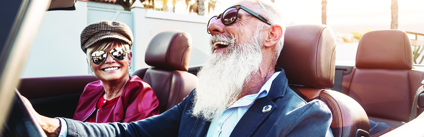 Older smiling couple with sunglasses sitting in a topless car.