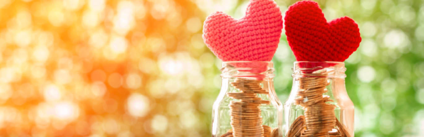 Two jars with coinsinside sit next two each other, capped by pink and red hearts.