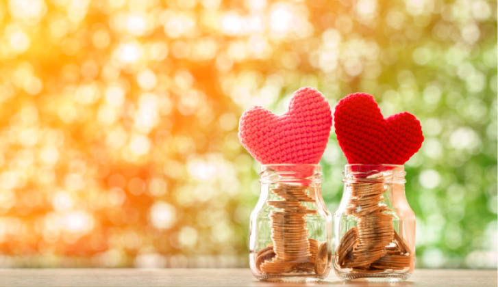 Two jars with coinsinside sit next two each other, capped by pink and red hearts.