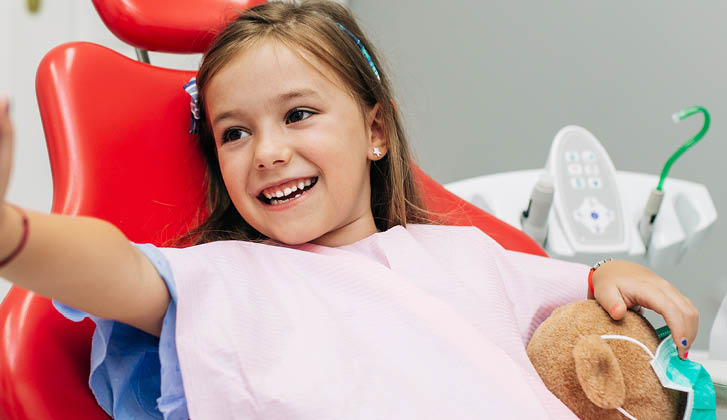 Child in a dentist chair, high-fiving a gloved hand with a smile in her face.