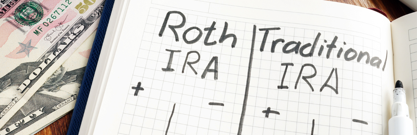 Notebook sitting on top of fifty dollar bills, the words Roth IRA and Traditional IRA written in marker