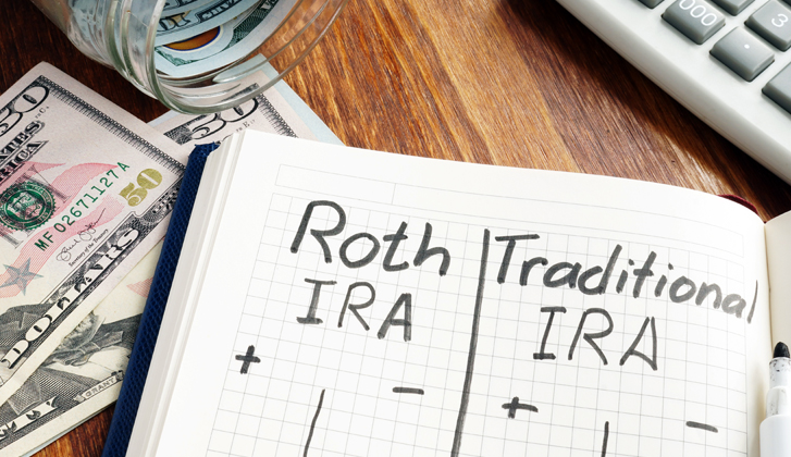 Notebook sitting on top of fifty dollar bills, the words Roth IRA and Traditional IRA written in marker