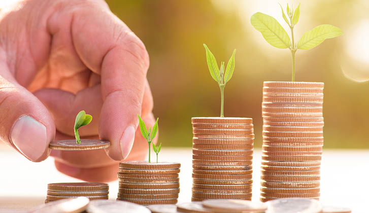 Stacks of quarters of varyin sizes with small plants growing out of them are being picked up by an index and thumb.