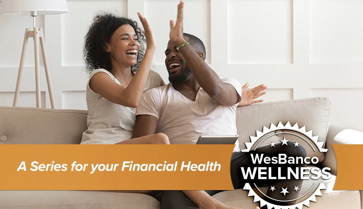 A young couple cheerfully high-five each other while sitting on a couch. The words A Series for your Financial Health in orange banner in the foreground.