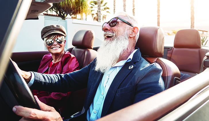 Older smiling couple with sunglasses sitting in a topless car.