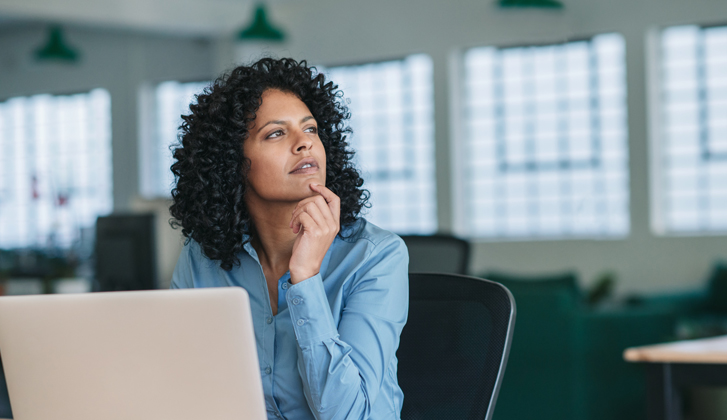 Young woman sittin in front of a computer looks away in thought.