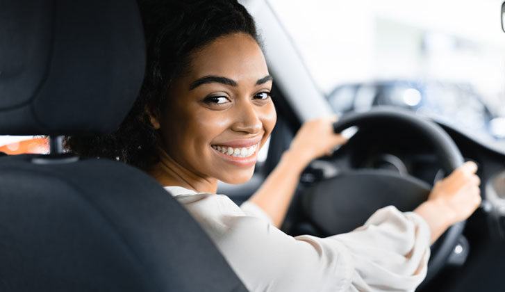 A smiling young woman looks back from the driver's seat.