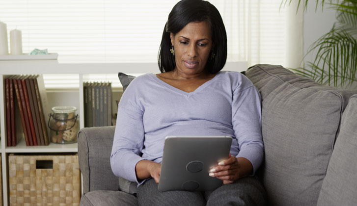 Woman relaxes on couch typing in a tablet.