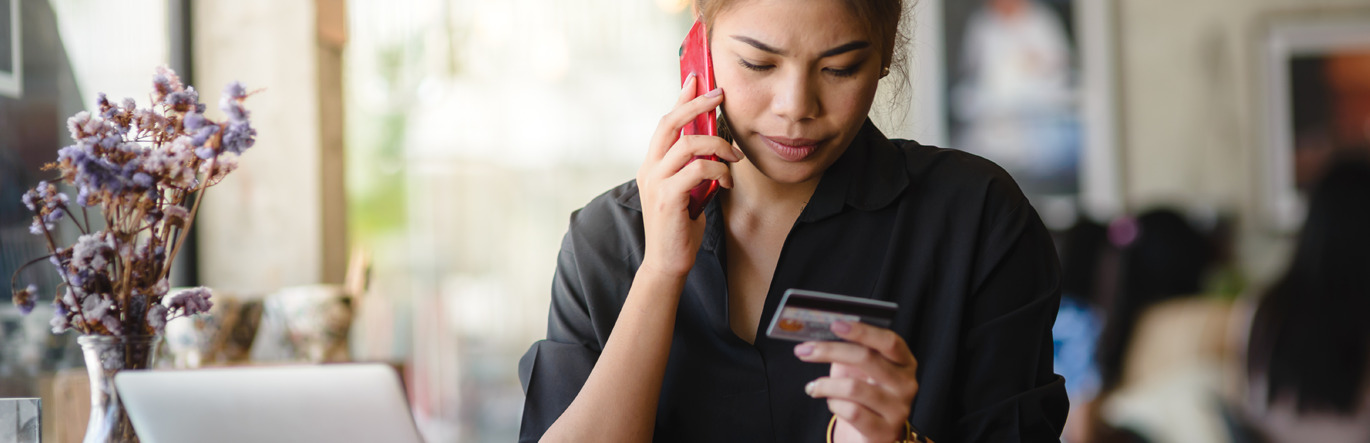 A young woman on the phone frowns down to the financial card in her hand.