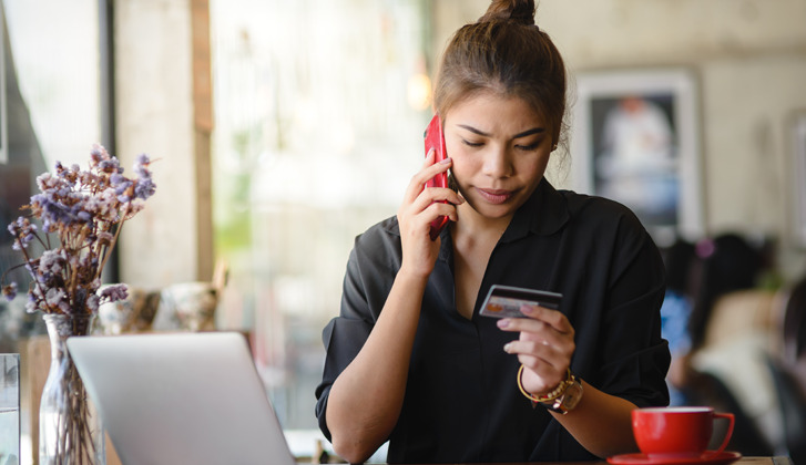 A young woman on the phone frowns down to the financial card in her hand.