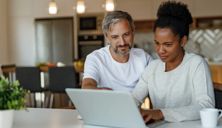 Couple working on a laptop in the kitchen.