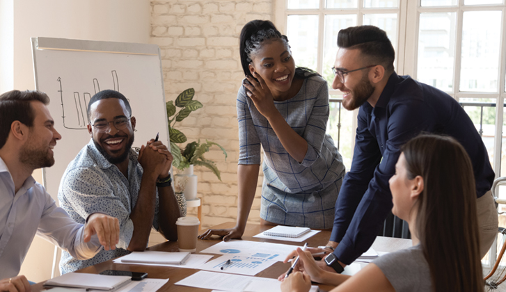 A group of young professionals animatedly discussing charts on an easel board behind them.