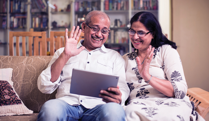 An older couple waves at someone in a video call on their tablet.
