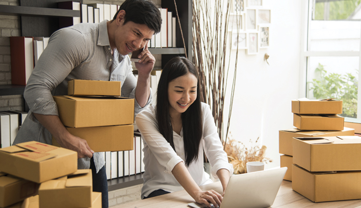 Young couple organize boxes and shipments from phone and computer.