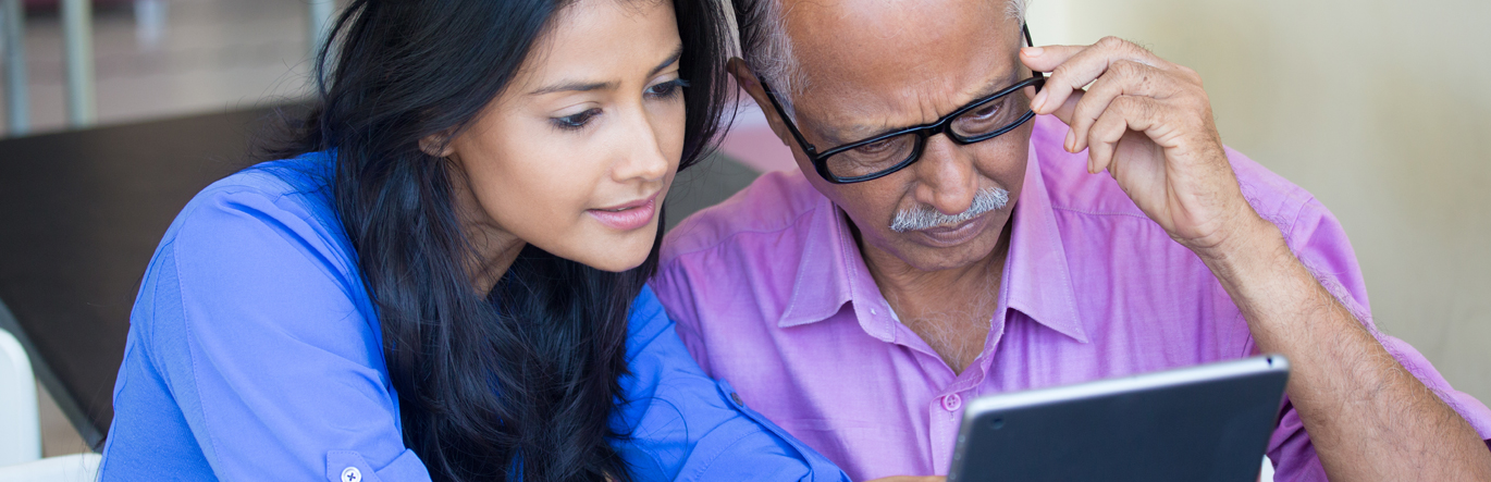Younger female explains document on digital device to older gentleman with glasses.