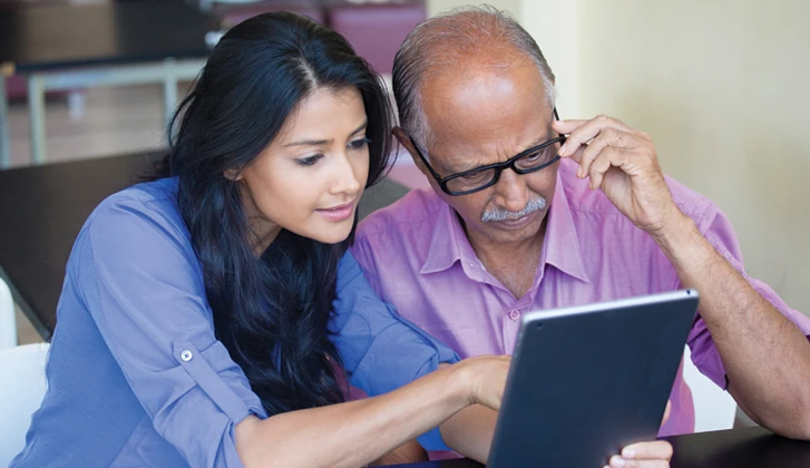 Younger female explains document on digital device to older gentleman with glasses.