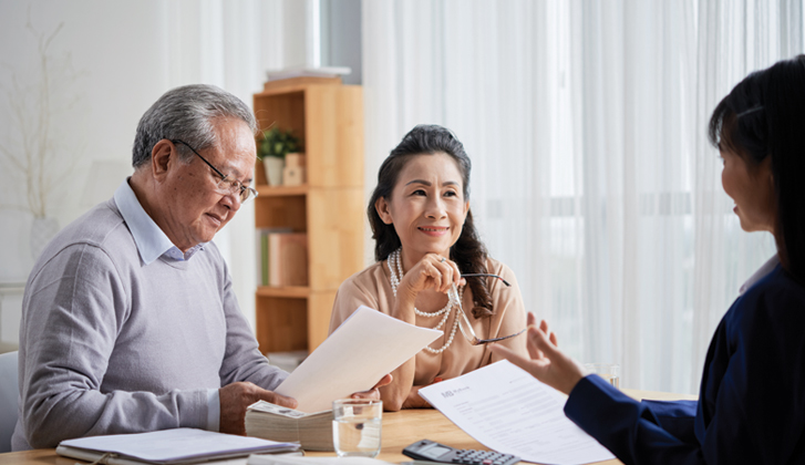 Elderly couple reviewing documents while an estate official explains.