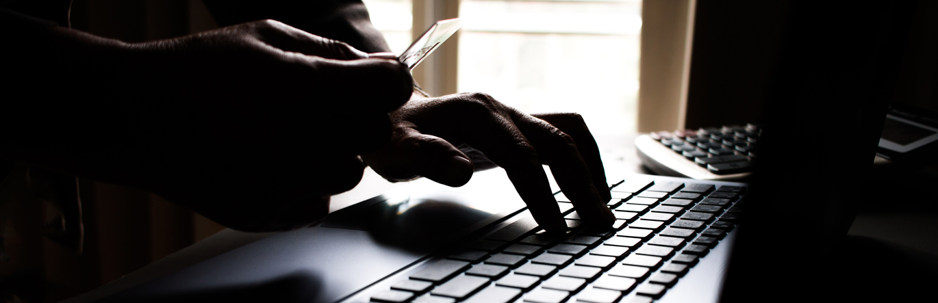 Disembodied hands hold a financial card and type information at the same time in the dark.