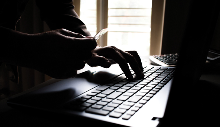 Disembodied hands hold a financial card and type information at the same time in the dark.