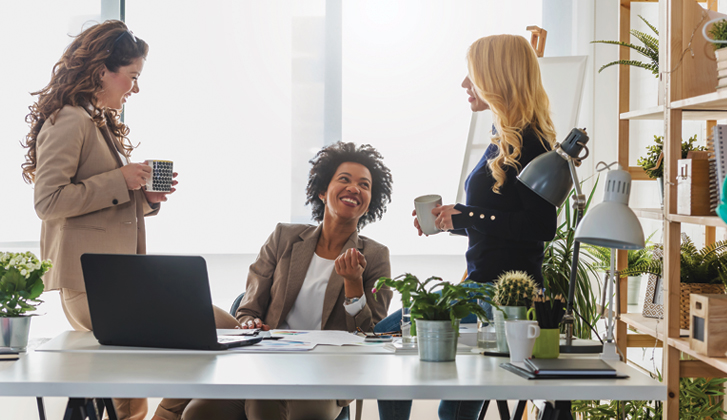 Three female businesswomen having coffe in a brightly-lit office.