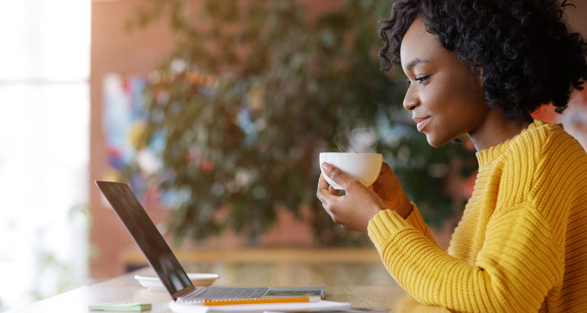 African American woman working from laptop while drinking from mug