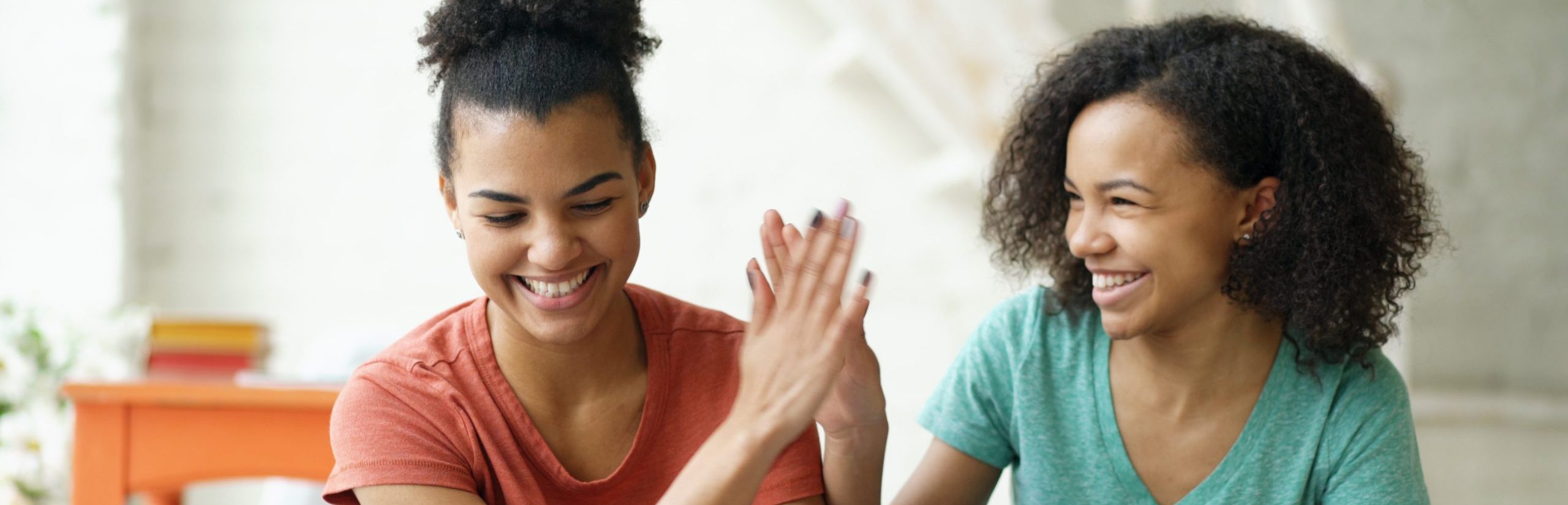 Two cheerful mixed race curly girlfriends shopping online with tablet computer and credit card at home
