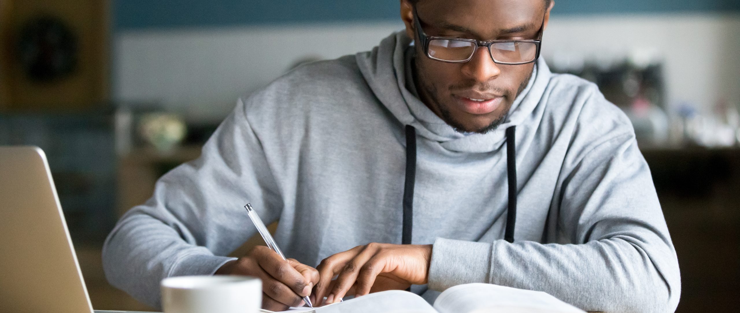 Closeup smart millennial african student wear glasses hold pen noting writing down information study use book preparing for university or college test exam, horizontal photo banner for website header