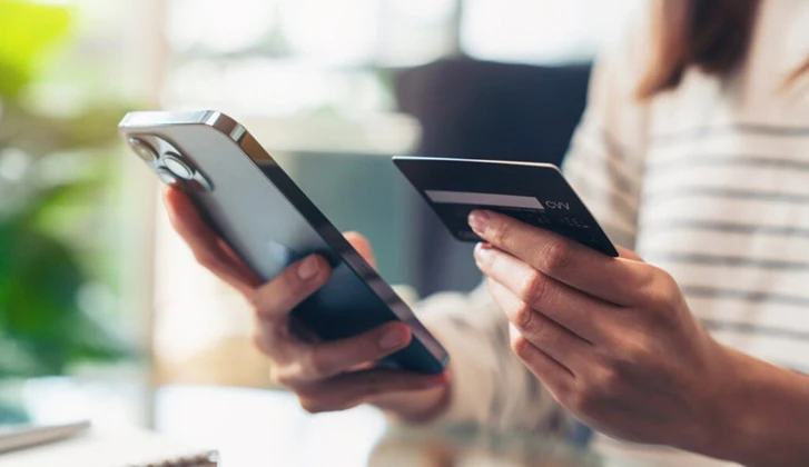 person holding credit card in one hand cell phone in other