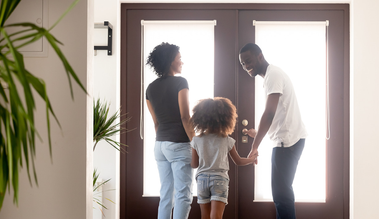 Family holding hands, about to walk through a door together.