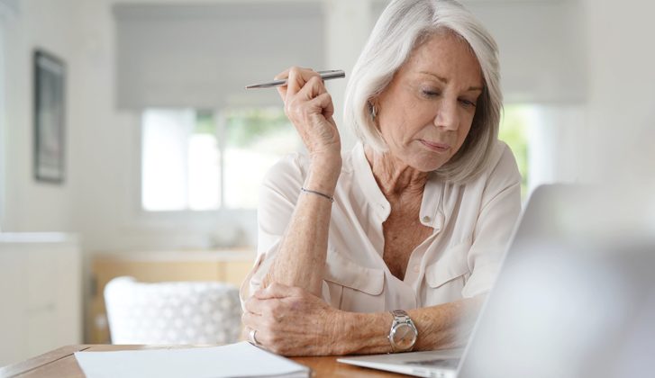 Elderly woman in thought while looking over documents and her computer.