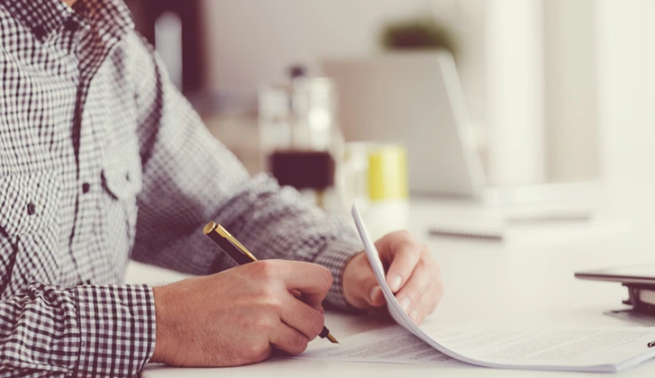 Man sitting at the table, holding a pen and signing contract. Focus on hands, unrecognizable person.