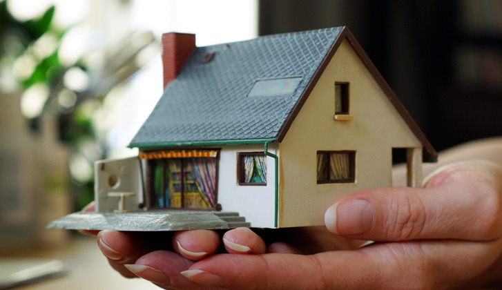 A woman's hands, cradling a toy house.