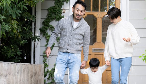 Young family helping their toddle walk in their backyard covered with greenery.