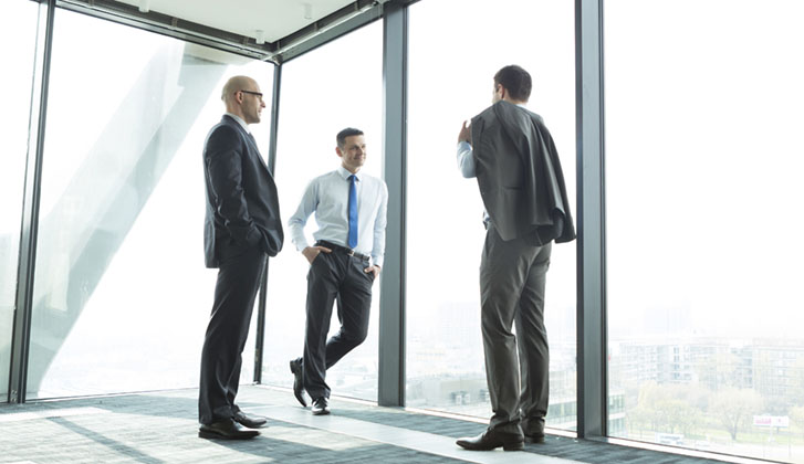 Three men in business suits having a conversation by corner windows
