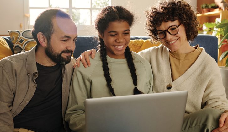Teen and her adoptive parents seated and smiling while looking at a laptop together.
