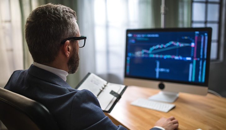 Man in suit and glasses looking at computer screen wtih line graphs