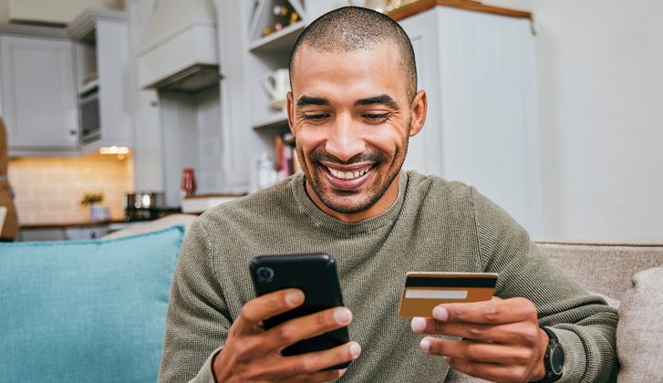 Smiling man holding cellphone and credit card.