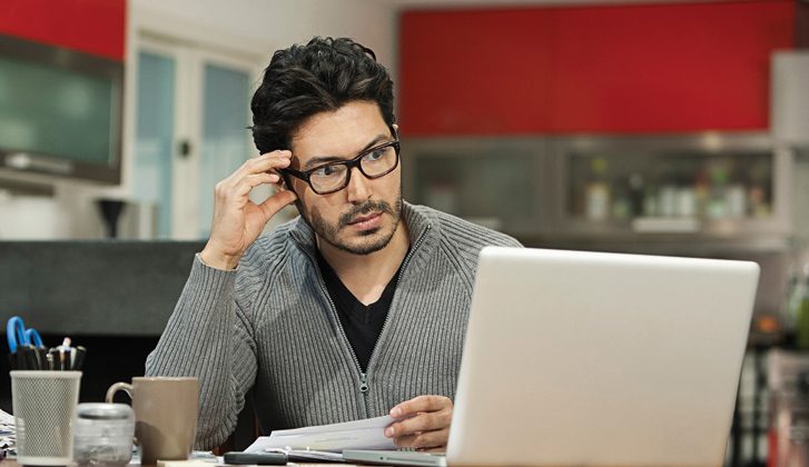 Man with glasses looks pensively at a computer screen.
