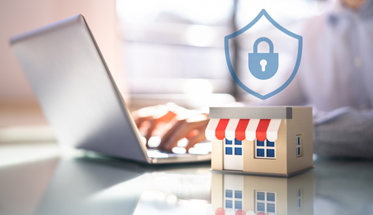 mini model of a storefront on a desk while a person in the background works on data security on their laptop