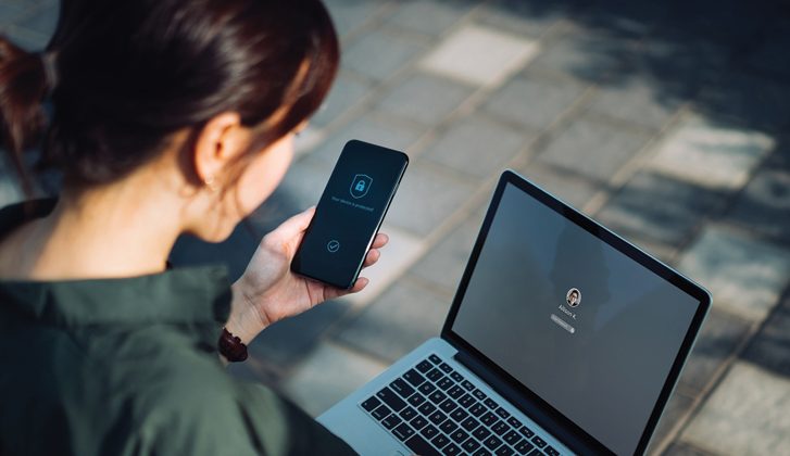 Woman completing two-factor authentication with her cellphone and laptop.