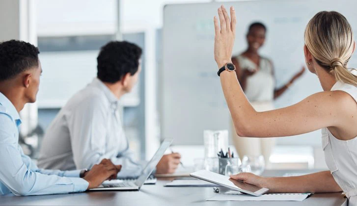 Work learning event; a woman raises her hand to ask a question.