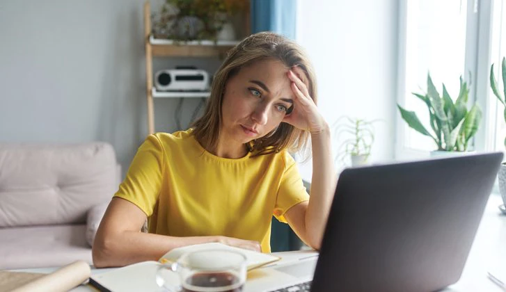 Woman looks pensively at a laptop. Her hand is on her forehead.