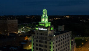 Clock tower style building in Youngstown Ohio with green lights highlighting the tower and an illuminated WesBanco logo